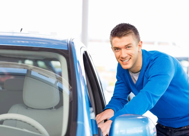 Young man smiling and leaning on new blue car