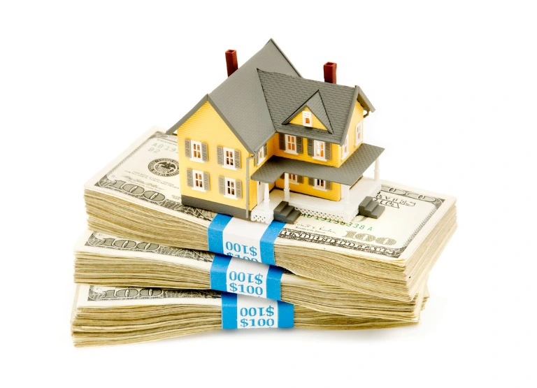 miniature house on top of stacks of money.