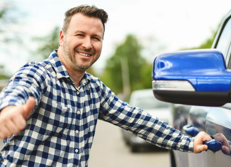 man smiling and giving thumbs up sign as he opens the door to new truck promoting auto loans from crossroads community fcu