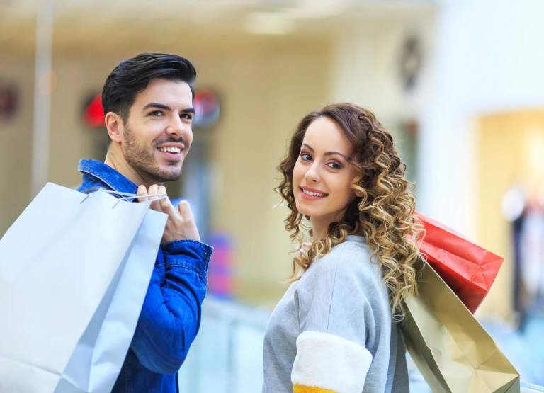 young couple holding shopping bags while look back at camera smiling