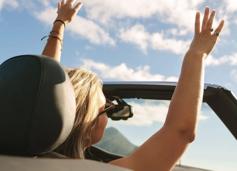 Woman in convertible car with hands in the air