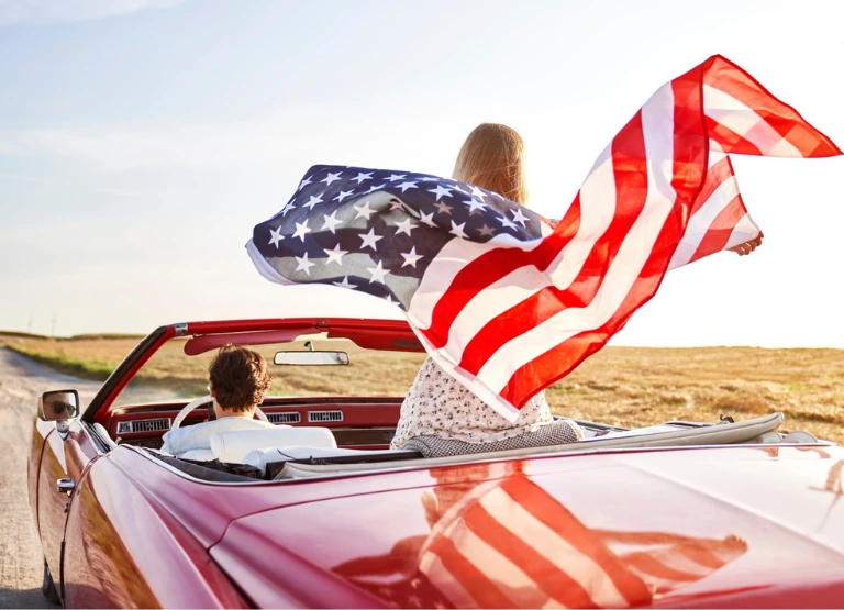 coupled driving in red convertible, woman standing and holding a flag