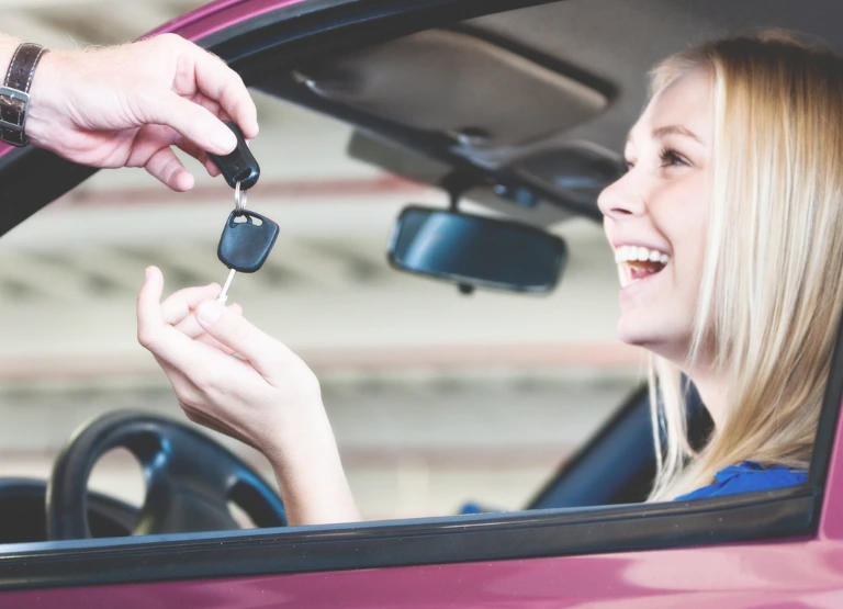 Young woman smiling and being handed car keys to new car