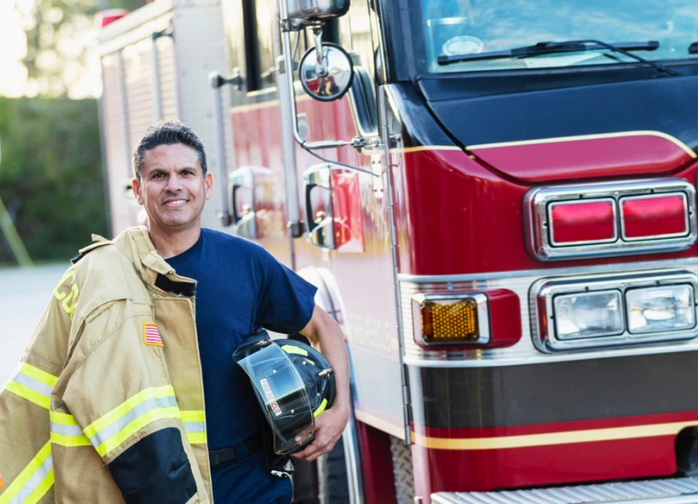 Fireman standing next to firetruck promoting crossroad community first responder rate of .25% off auto and personal loans